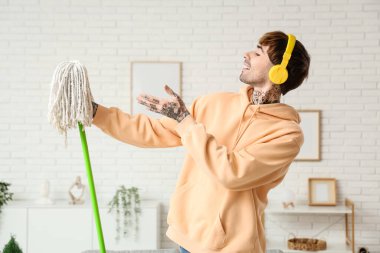 Genç dövmeli adam evini temizlerken paspasla dans ediyor.