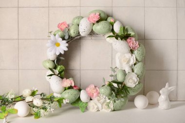 Küçük tavşancık, güzel Paskalya çelengi çiçeklerle süslenmiş ve arka planda yumurtalar.