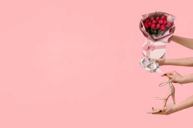 Bir buket lale, yüksek topuklu ayakkabı ve pembe arka planda hediye kutusu olan kadın elleri. Uluslararası Kadınlar Günü için Alışveriş