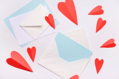 Boş kartlı zarflar ve beyaz arka planda kırmızı kağıt kalpler. Sevgililer Günü kutlaması