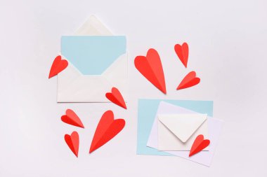 Boş kartlı zarflar ve beyaz arka planda kırmızı kağıt kalpler. Sevgililer Günü kutlaması