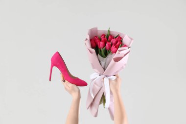 Pembe lale buketi ve beyaz arka planda yüksek topuklu ayakkabısı olan kadın elleri. Uluslararası Kadınlar Günü için Alışveriş
