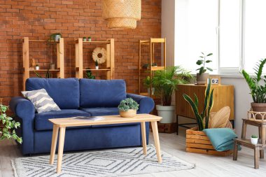 Oturma odasının içinde kanepe, raf üniteleri, masa ve ev bitkileri var.