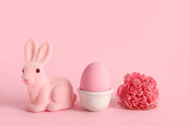 Boyanmış Paskalya yumurtası, pembe arka planda tavşan ve şakayık çiçeği olan tutucu.