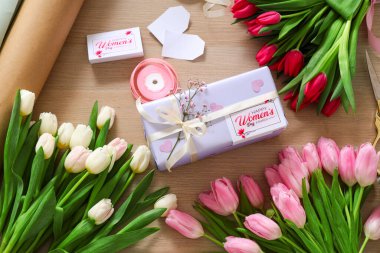 Ahşap zemin üzerinde Uluslararası Kadınlar Günü için hediye paketi, paketleme malzemeleri ve güzel lale çiçekleri olan kompozisyon