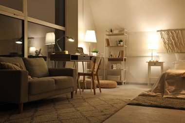 Yatak odasının içi, iş yeri, kanepe ve gece lambalarıyla dolu.