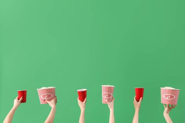 Patlamış mısırlı kovaları tutan eller ve yeşil arka planda içkiler