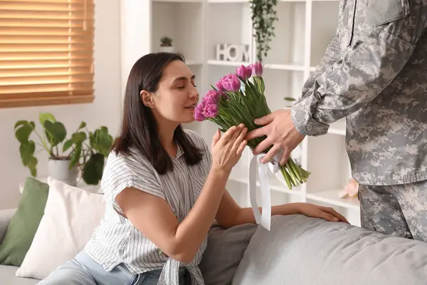 Man in military uniform greeting his wife with bouquet of flowers at home. Valentine\'s Day celebration
