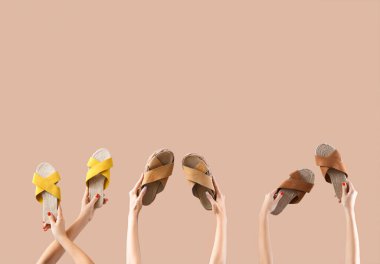 Bej arka planda farklı sandaletler tutan kadın eller.