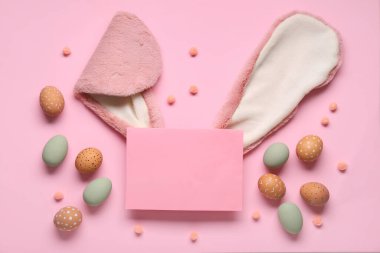 Tavşan kulakları, Paskalya yumurtaları ve pembe arka planda boş bir kart. Üst görünüm