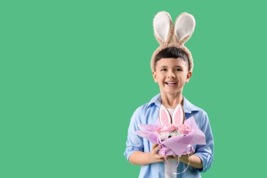 Yeşil arka planda Paskalya pastası olan tavşan kulağı takan şirin bir çocuk.