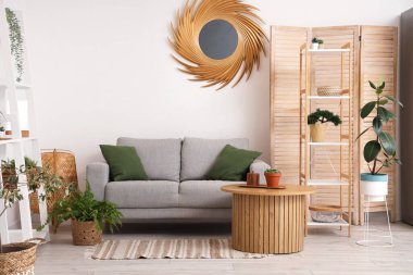 Oturma odasının içinde raf üniteleri, ev bitkileri, ayna, masa ve kanepe.