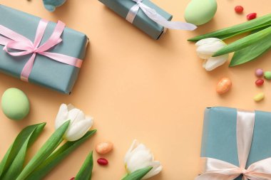 Paskalya yumurtaları, lale çiçekleri ve turuncu arka planda hediye kutuları.