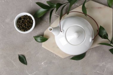 Çaydanlıklı bir pano, bir kase kuru çay ve gri arkaplanda yapraklar.