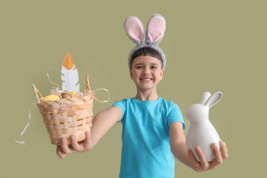 Paskalya sepetiyle tavşan kulağı takan sevimli küçük çocuk ve yeşil arka planda tavşan.
