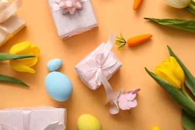 Lale çiçekli Paskalya yumurtaları ve turuncu arka planda hediye kutuları.