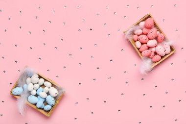 Paskalya yumurtaları ve pembe arka planda tüyleri olan kutular
