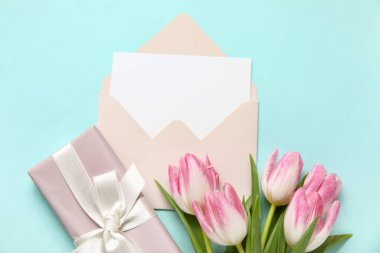 İçinde boş kart, hediye kutusu ve mavi arka planda pembe laleler olan zarf.