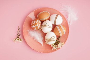 Süslü Paskalya yumurtaları, küçük çiçekler ve pembe arka planda tüylerle kaplı bir tabak.