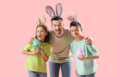 Pembe arka planda Paskalya yumurtaları olan küçük çocuklar ve tavşan kulaklı babası.