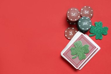 Poker fişleri, bir deste kağıt ve kırmızı arka planda şanslı yoncalar. Aziz Patrick Günü kutlaması