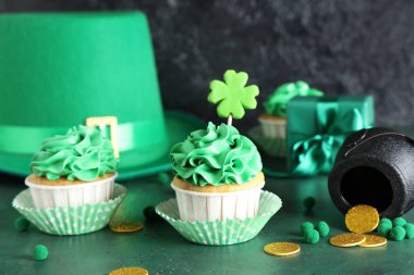 Lezzetli kapkekler, leprikon şapkalı ve dekorlu. St. Patrick Günü için yeşil grunge masasında, siyah arka planda.