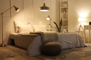 Rahat yatağın üzerinde yumuşak battaniyeler, hasır puf ve geceleri parlayan lambalar olan rahat yatak odasının içi.