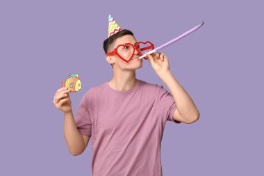 Mor arka planda düdük ve kağıt balıkla komik kılık değiştirmiş yakışıklı bir genç. 1 Nisan kutlamaları