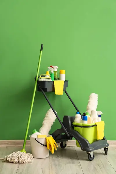 Trolley with cleaning supplies near green wall