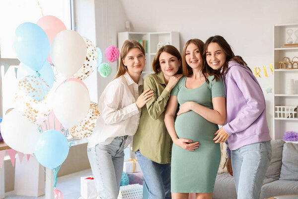 Молодая беременная женщина с друзьями, обнимающимися на вечеринке в честь рождения ребенка