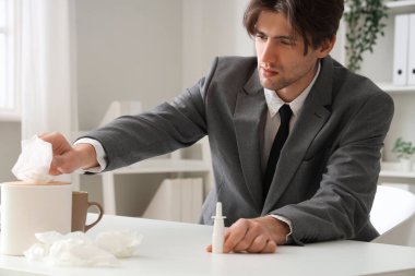 Burun damlası olan hasta işadamı ofisteki kutudan mendil alıyor.