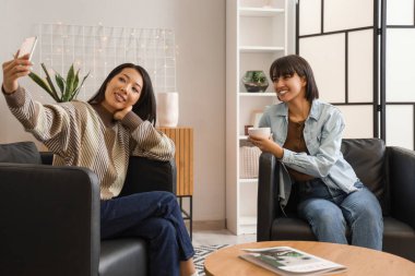 Siyah koltuklu genç kadınlar evde selfie çekiyorlar.