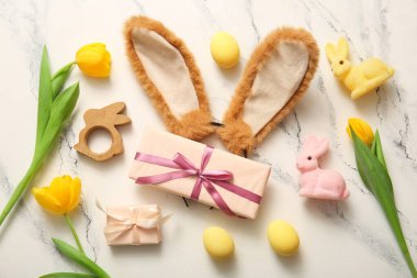 Paskalya yumurtalı tavşan kulakları, hediye kutuları ve beyaz mermer arka planda lale çiçekleri.