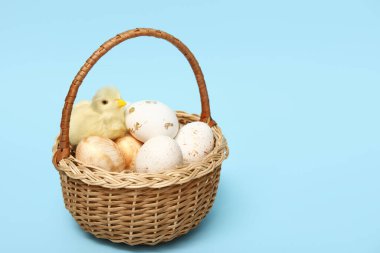 Mavi arka planda Paskalya yumurtası ve tavuk heykelciği olan sepet.