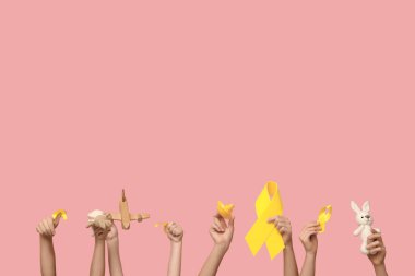 Çocuk elleri pembe arka planda oyuncakları ve sarı kurdeleleri tutuyor. Uluslararası Çocukluk Kanser Günü