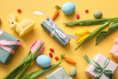 Hediye kutularıyla Paskalya yumurtaları, lale çiçekleri ve turuncu arka planda tavşan.