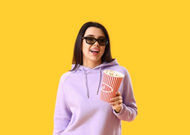 Patlamış mısır ve 3D gözlüklü güzel bir kadın sarı arka planda film izliyor.