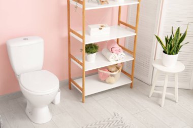 Pembe duvarın yanında seramik klozeti olan şık bir banyo.