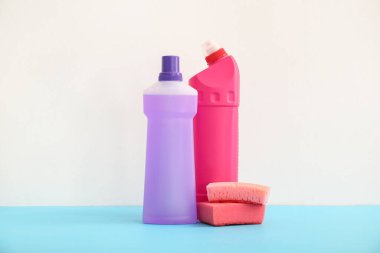 Mavi masada beyaz arka planda deterjan ve sünger şişeleri