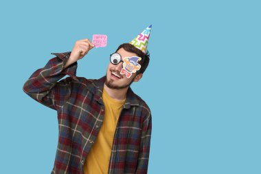 Mavi arka planda çıkartmaları olan komik görünümlü yakışıklı bir genç. 1 Nisan kutlamaları