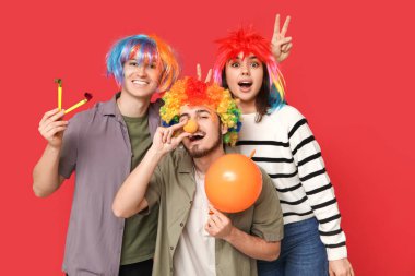 Kırmızı arka planda parti düdüğü ve balonla komik kılık değiştirmiş genç arkadaşlar. 1 Nisan kutlamaları