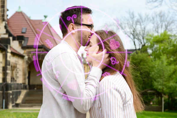 Drawn Zodiac signs and young man kissing his girlfriend outdoors. Love compatibility horoscope. Partner matching by date of birth