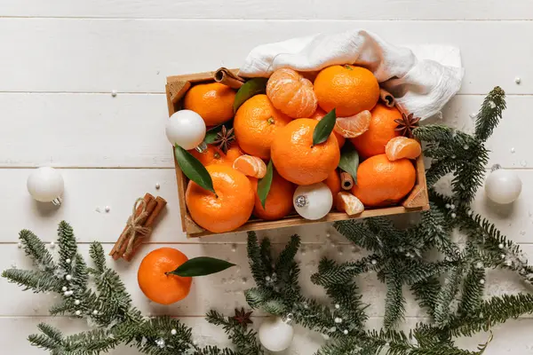 Tarçınlı bir kutu tatlı mandalina, yıldız anason, Noel topları ve beyaz ahşap arka planda köknar dalları.