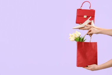 El çantalı kadın eller, yüksek topuklu ayakkabılar ve leylak arka planda laleler. Uluslararası Kadınlar Günü için Alışveriş