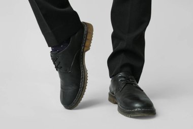 Gri arka planda siyah şık ayakkabılı genç adamın bacakları.