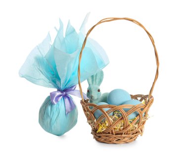 Beyaz arka planda boyanmış Paskalya yumurtaları, oyuncak tavşan ve hediye çantasıyla hasır sepet.