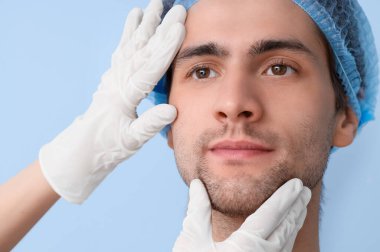 Mavi arka planda estetik cerrahı olan yakışıklı genç adam, yakın plan.