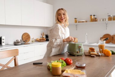Genç, güzel, mutlu bir kadın mutfakta lezzetli tostlar yapıyor.