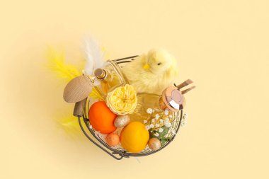 İçinde parfüm şişeleri olan sepet, Paskalya yumurtası ve sarı arka planda yavru tavuk.