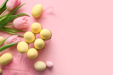 Boyanmış Paskalya yumurtaları, lale çiçekleri ve pembe arka planda tüyleri olan tutucu.